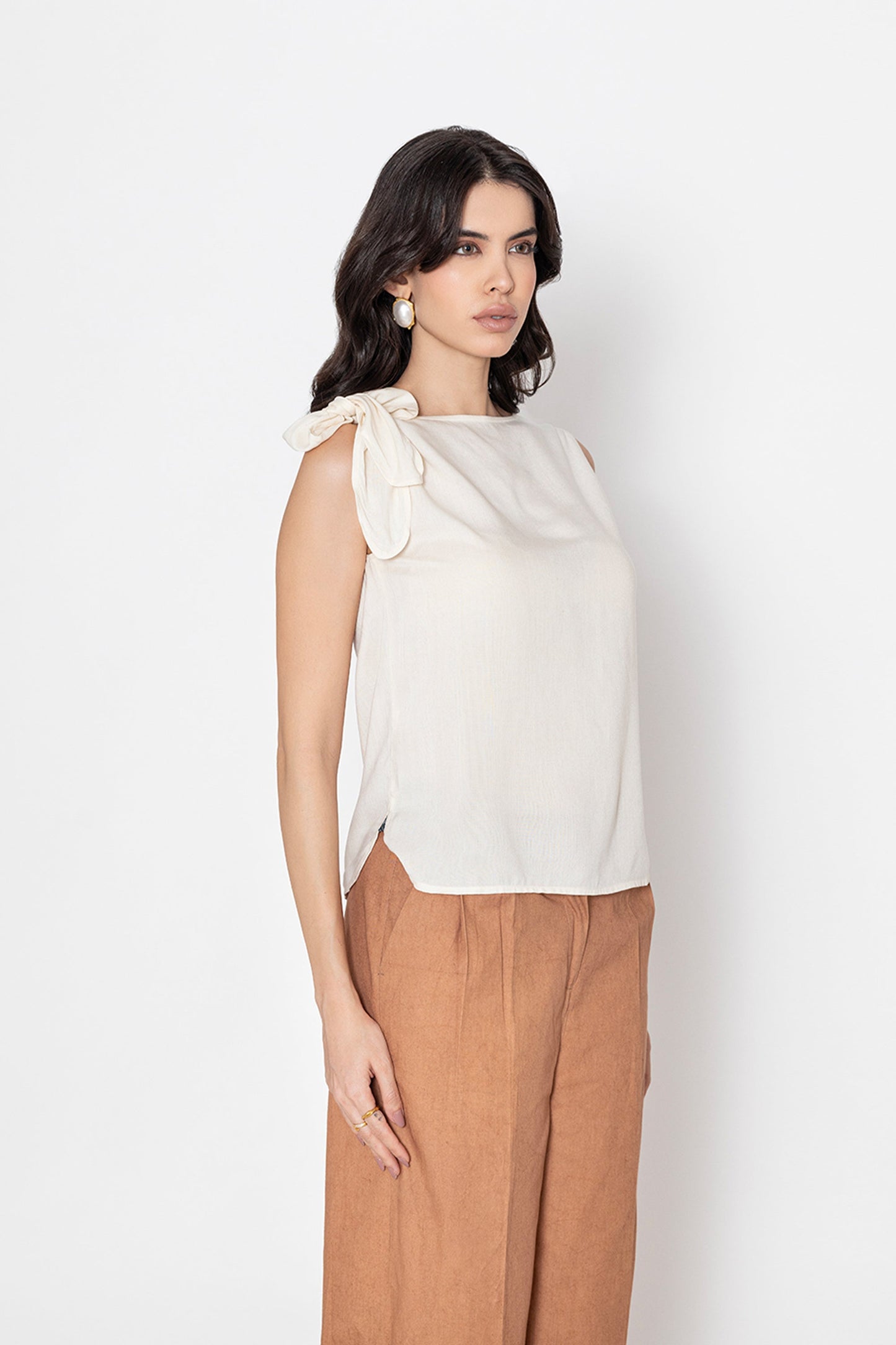 white sleeveless blouse with bow detail on shoulder worn with brown pants