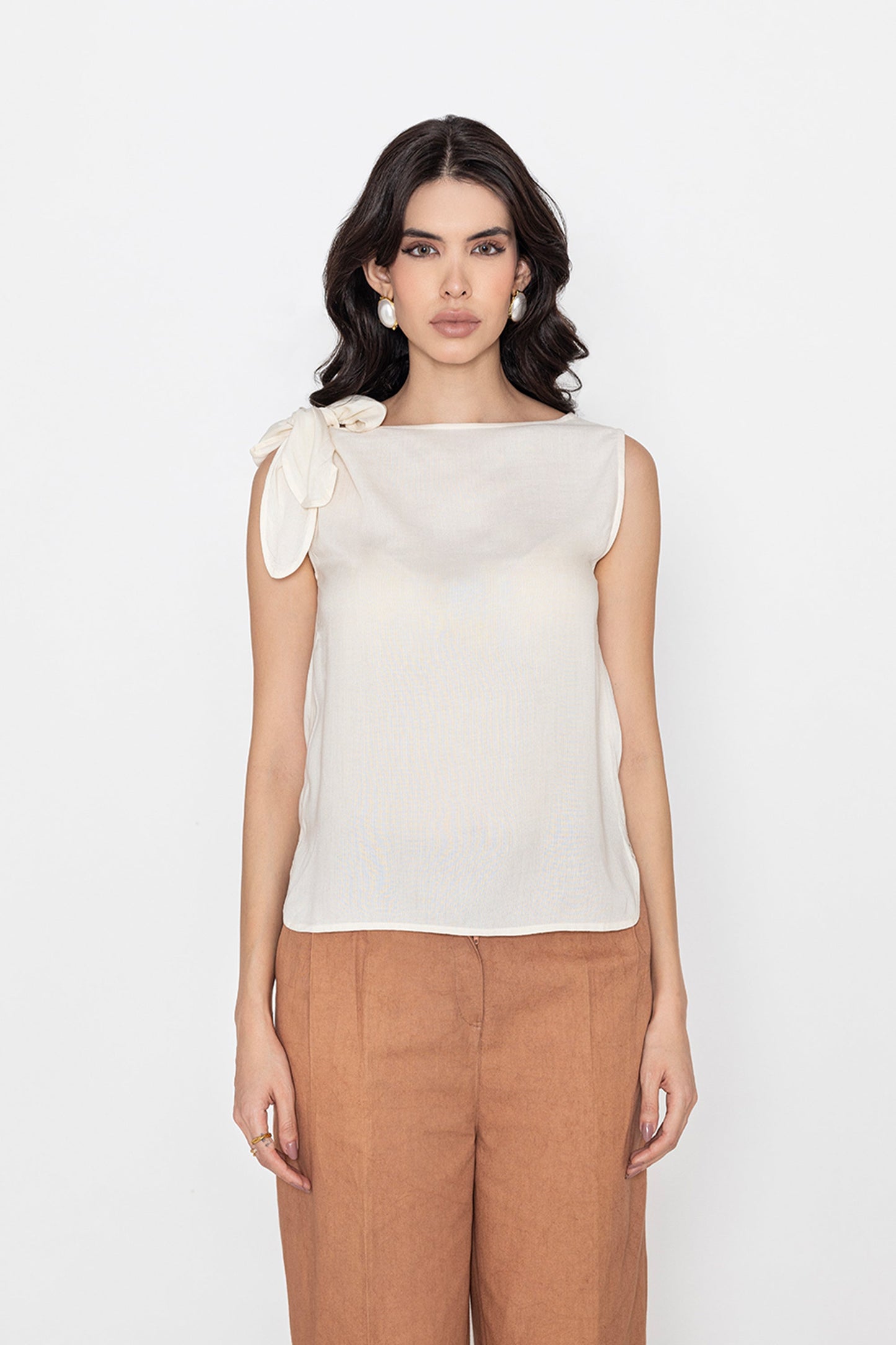 white sleeveless blouse with bow detail on shoulder styled with brown pants