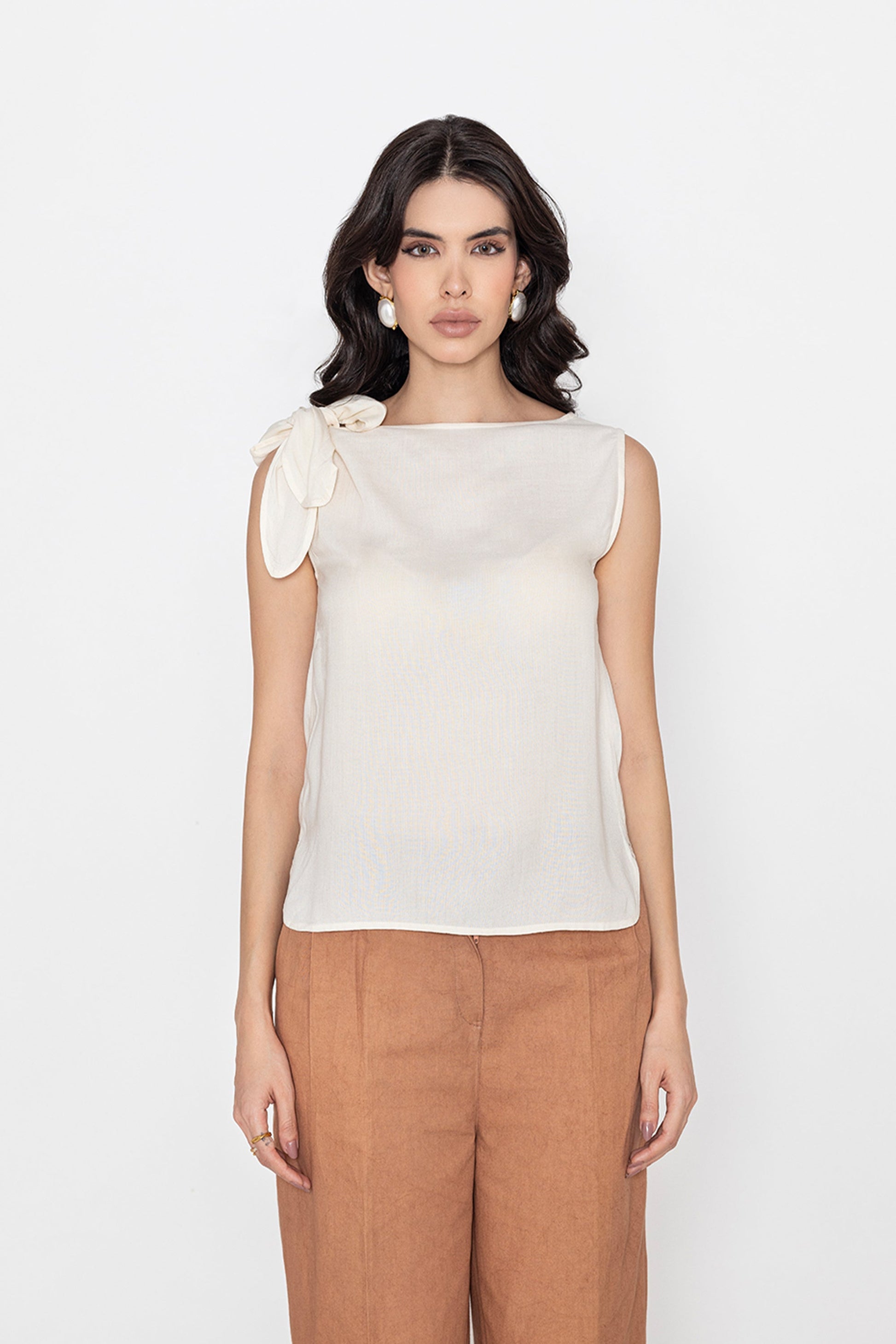 white sleeveless blouse with bow detail on shoulder styled with brown pants