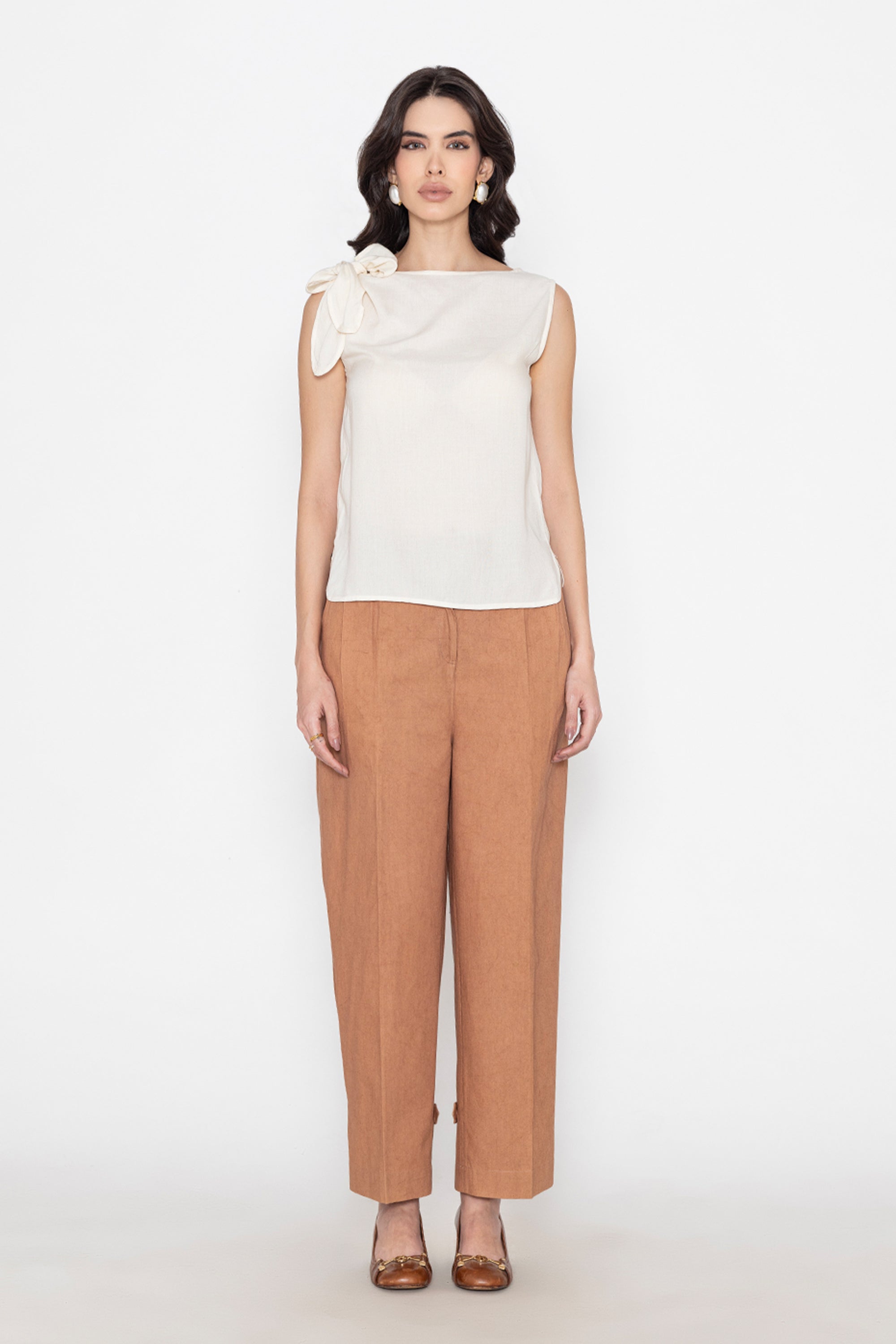 white sleeveless blouse with bow detail paired with brown pants