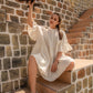 Model wearing a white summer dress for women while holding a vintage airplane on outdoor stairs