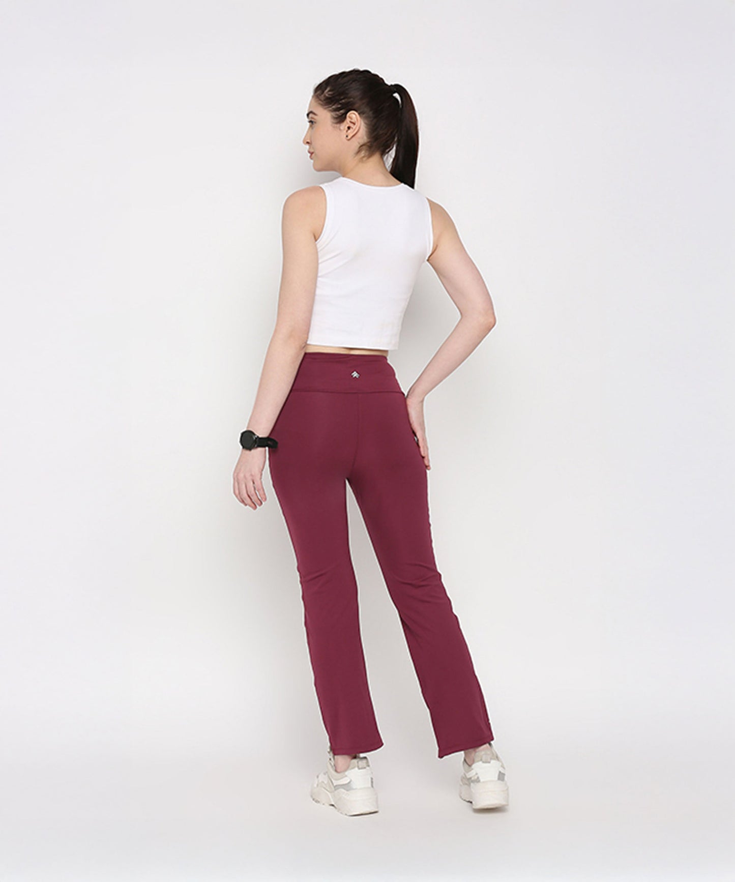 Back view of a model wearing a white twisted crop top paired with maroon activewear pants from Stylera