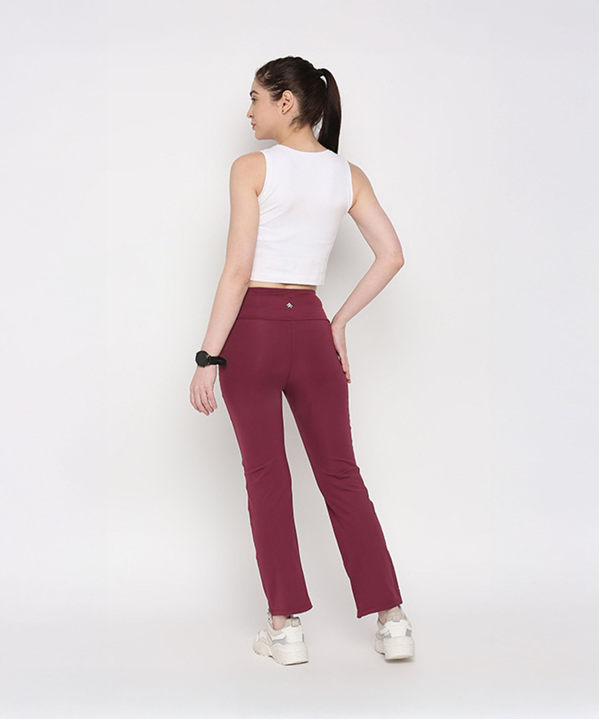 Back view of a model wearing a white twisted crop top paired with maroon activewear pants from Stylera