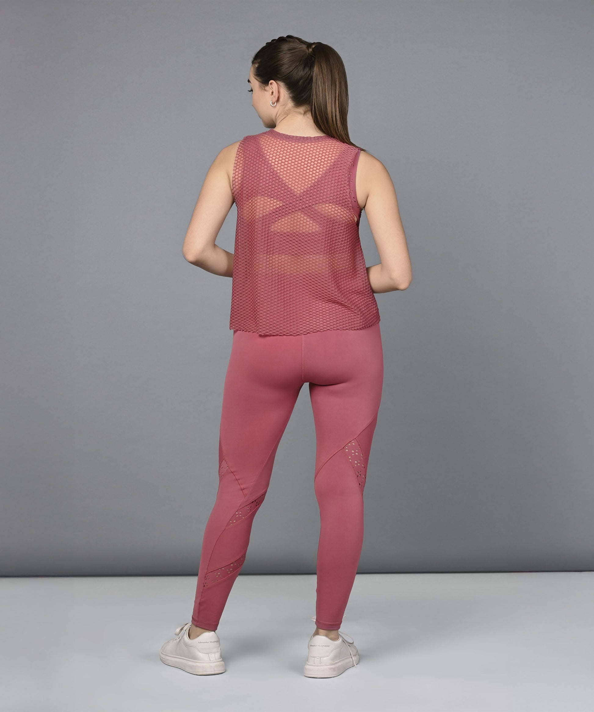 Back view of a woman wearing a pink women's mesh workout top with matching leggings for active fitness.