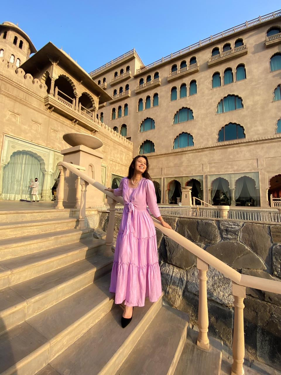 Model in a pink women's elegant long dress standing on stairs at a stunning historic venue
