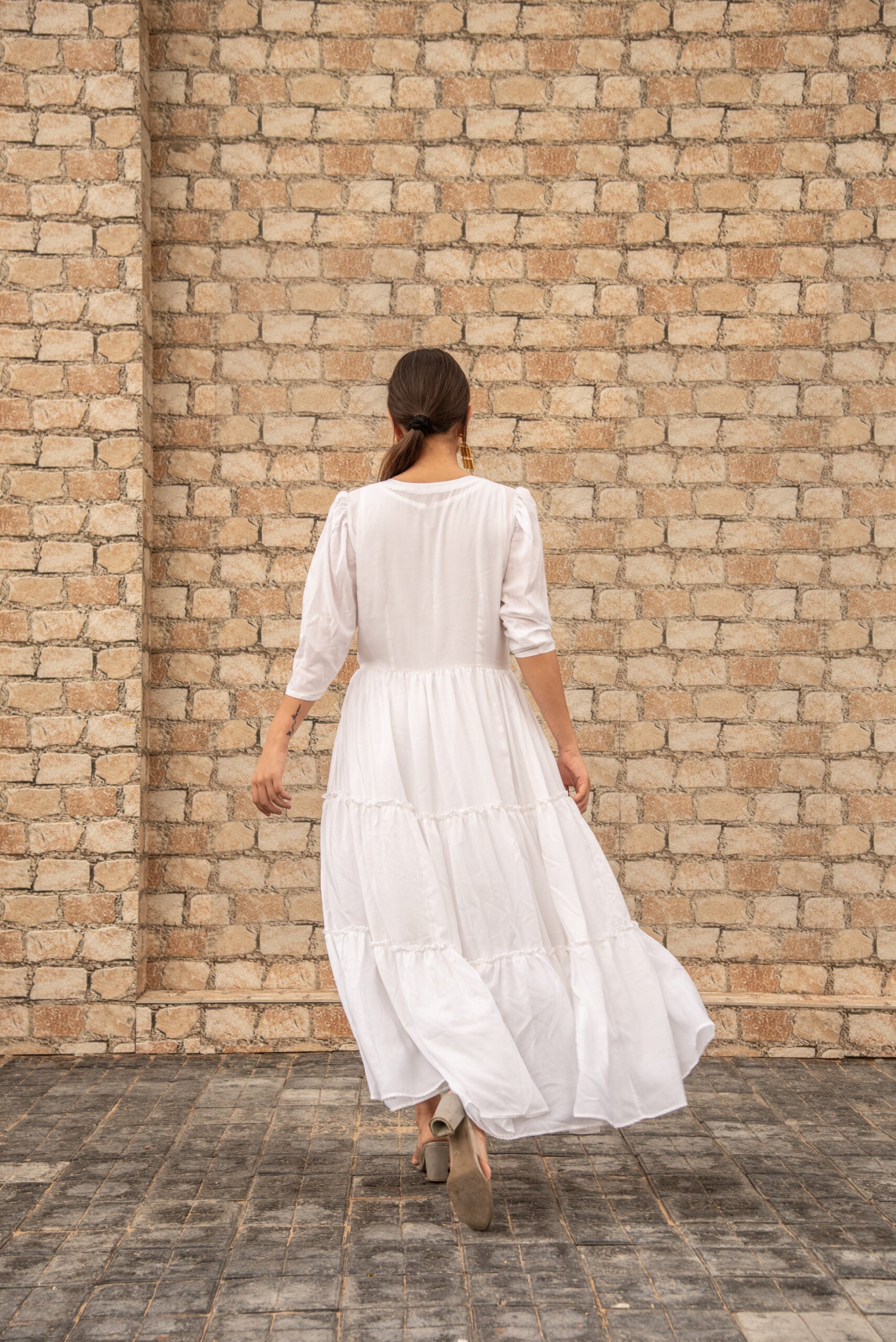Back view of a women's elegant long dress by Stylera, featuring a flowy silhouette and tiered design