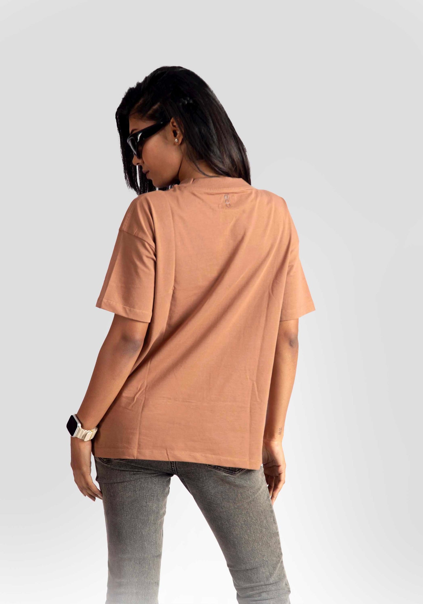 Back view of woman wearing womens graphic oversized mocha tee paired with gray jeans and sunglasses