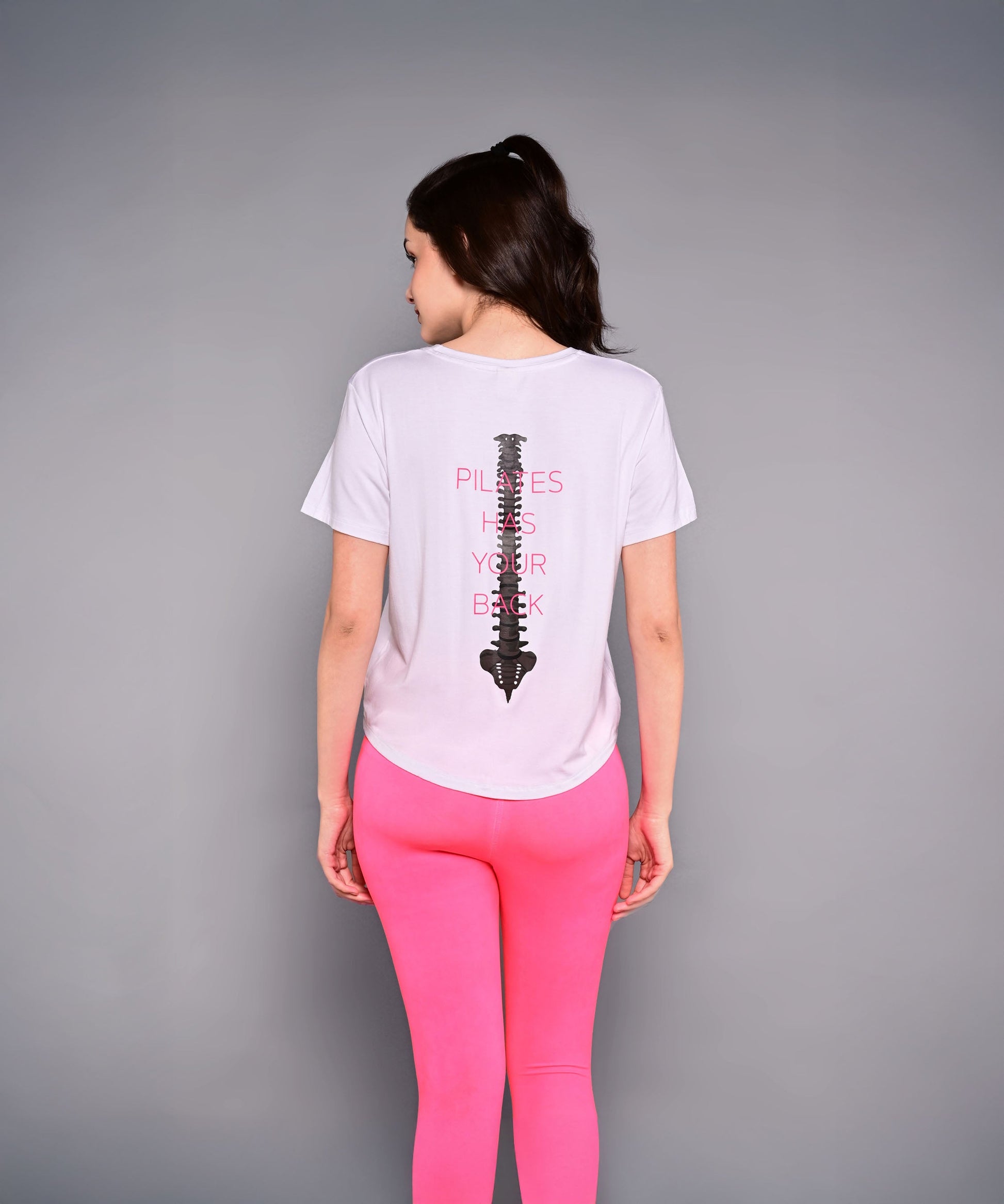 Back view of a women's Pilates exercise top with spine graphic in pink and white design