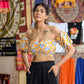 Woman wearing yellow floral off shoulder crop top paired with black pants in a colorful market setting