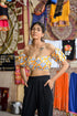 Woman wearing yellow floral off shoulder crop top paired with black pants in a colorful market setting