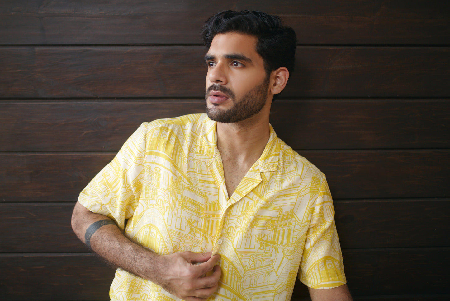 Stylish model wearing a yellow oversize shirt for men with a trendy pattern against a dark wood background