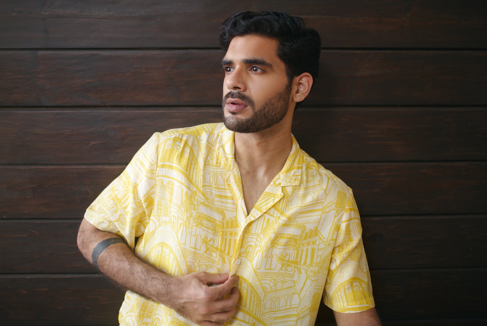 Stylish model wearing a yellow oversize shirt for men with a trendy pattern against a dark wood background