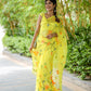 Elegant yellow saree with floral print, perfect for festive occasions, modeled in a lush garden setting