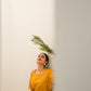 Woman wearing a yellow summer midi dress standing against a white wall with greenery above her head